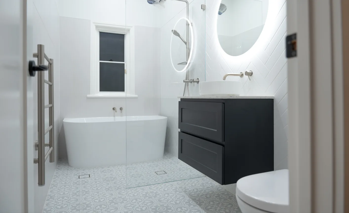 Renovated bathroom with freestanding bath, black vanity and round backlit mirror