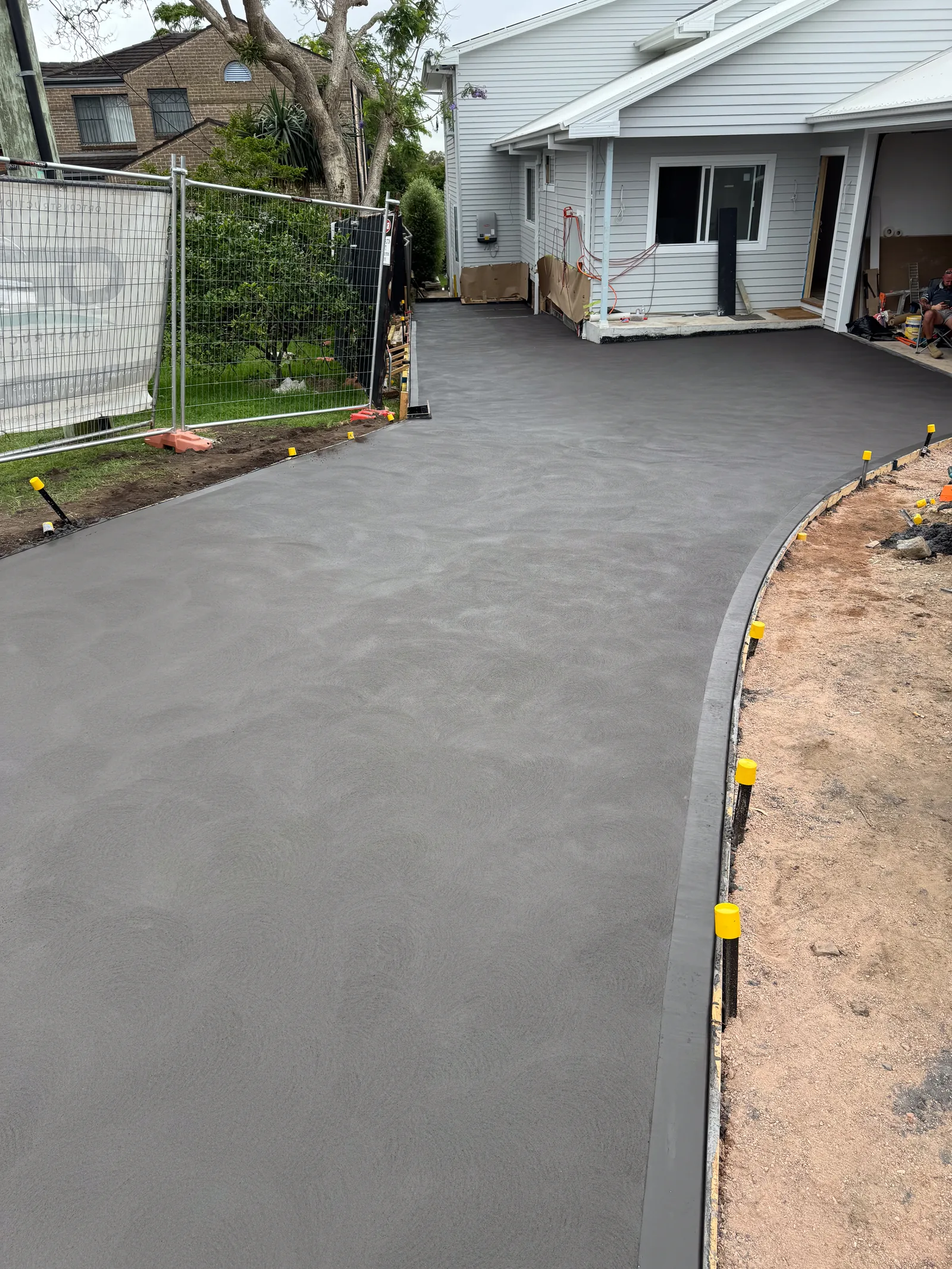 Newly poured and finished concrete driveway with a formed kerb edge running beside a house