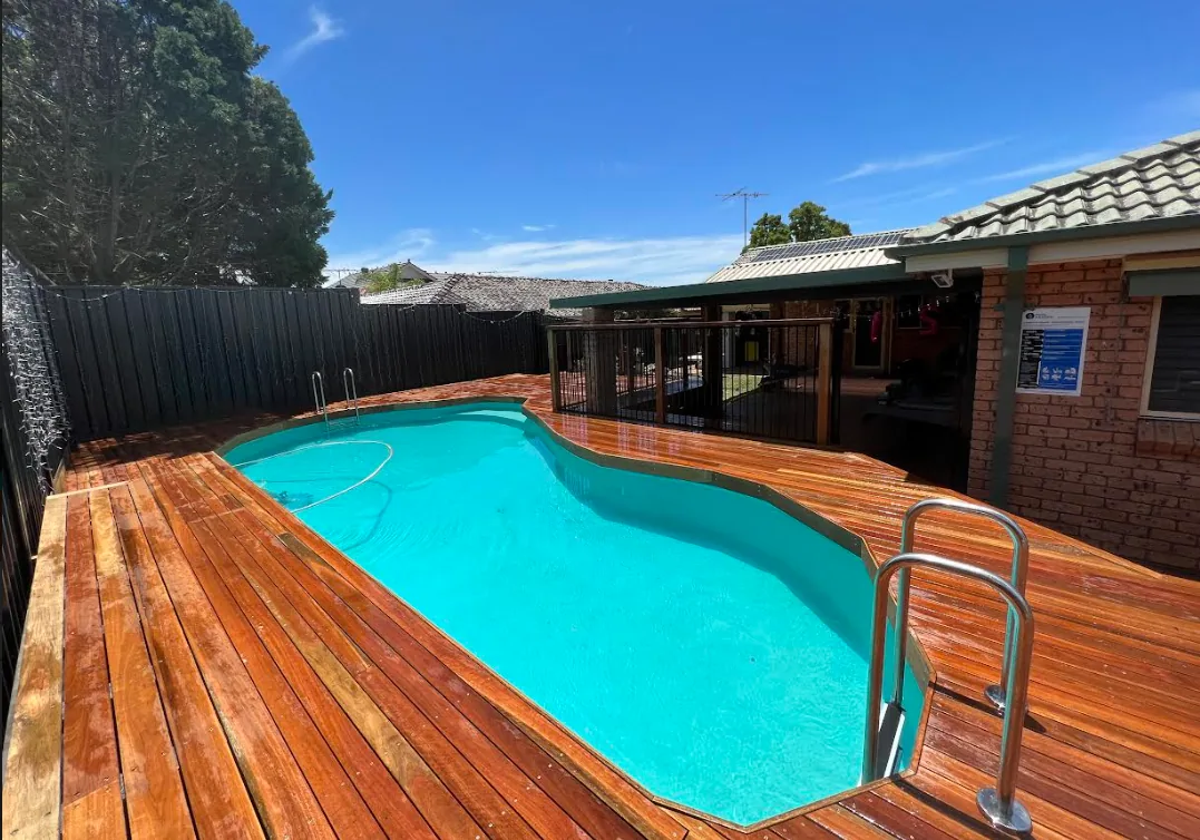 Hardwood deck laid around an inground pool with a covered outdoor area against the brick house