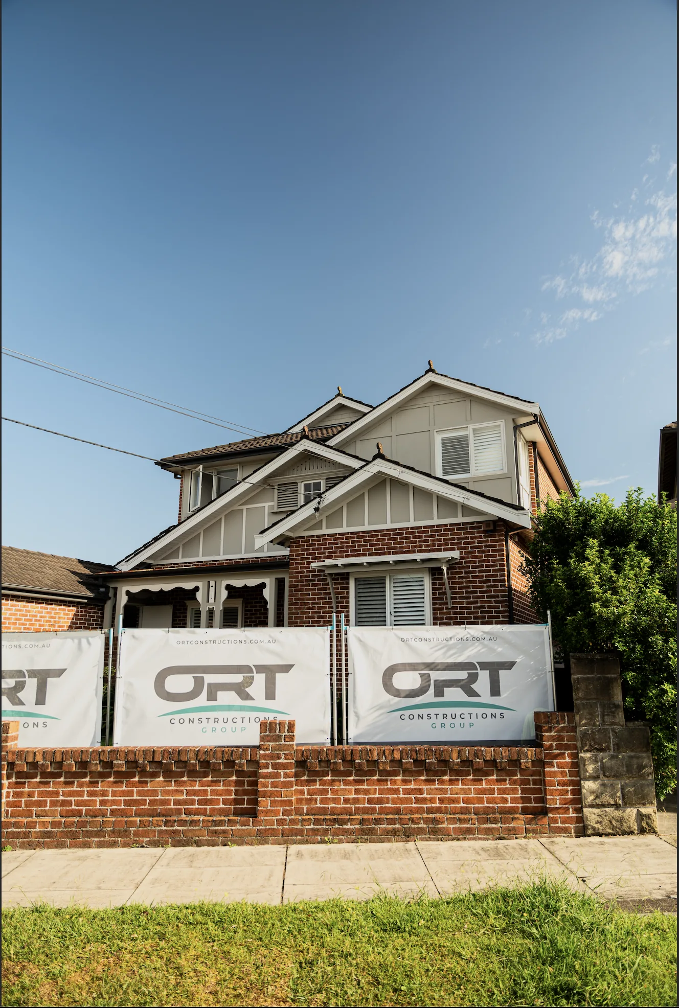 Front facade of a renovated home with ORT Constructions site banners on the fence