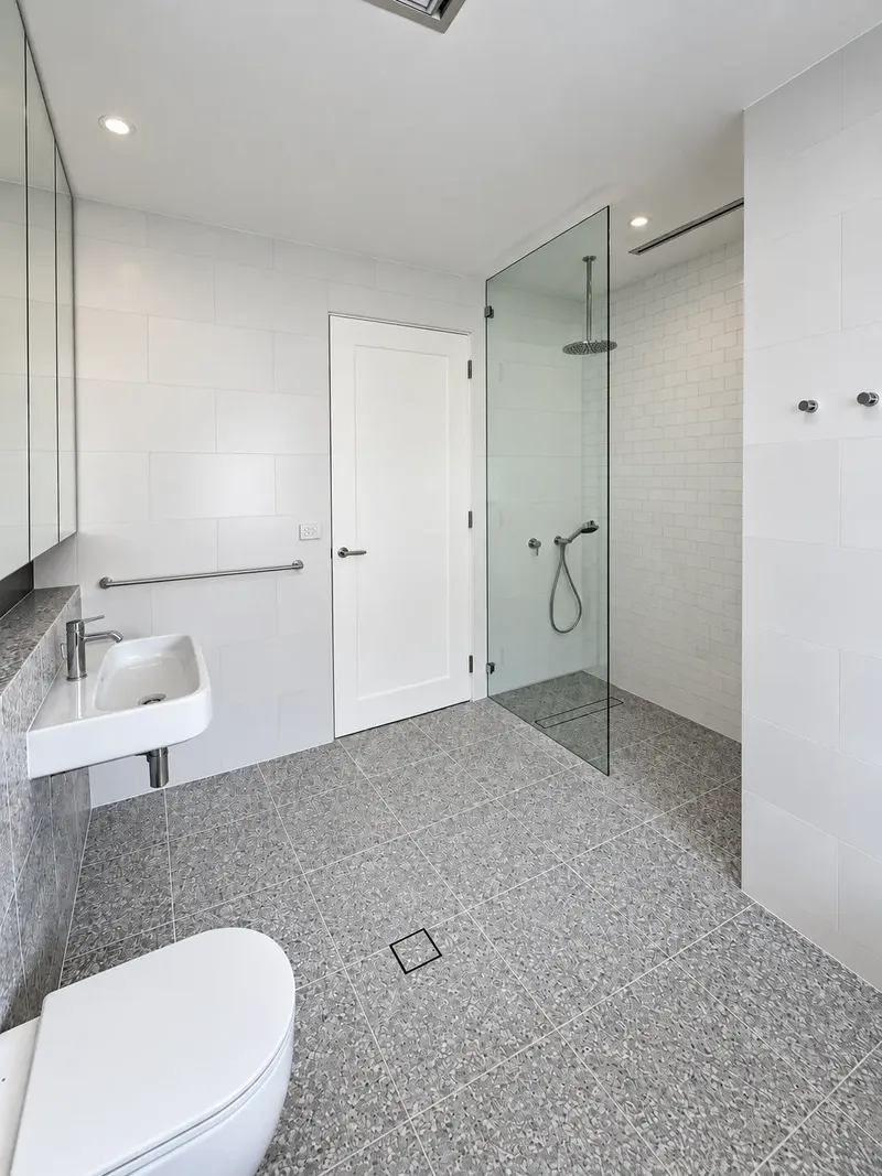 Finished bathroom with frameless shower screen, floor-to-ceiling tiling and stone vanity