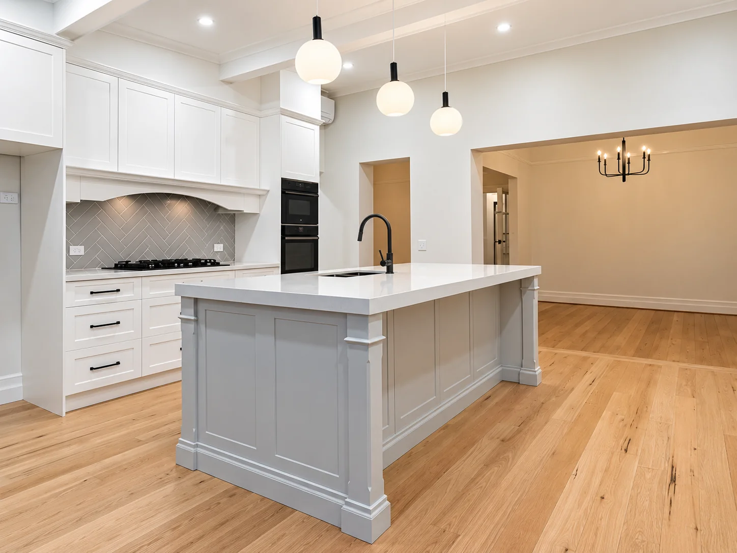 White shaker kitchen with stone island bench, herringbone splashback and timber flooring at Russell Lea