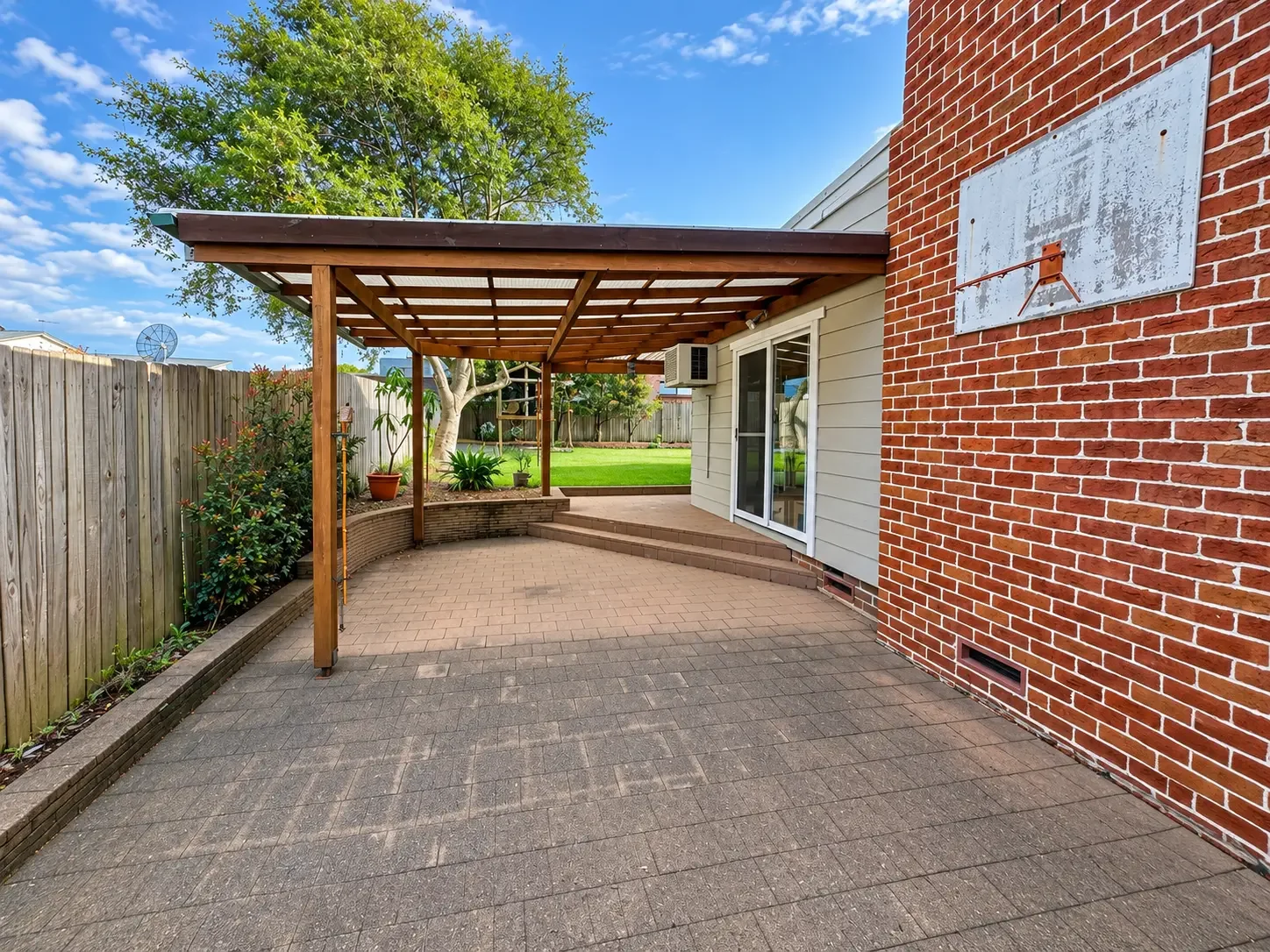 Covered timber pergola over paved patio beside the brick home at Russell Lea