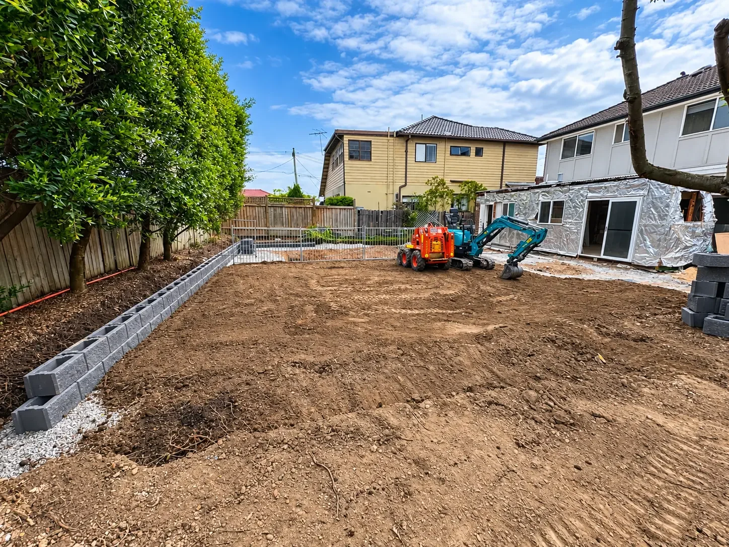 Excavated and levelled site prepared for construction with a compact excavator in the background