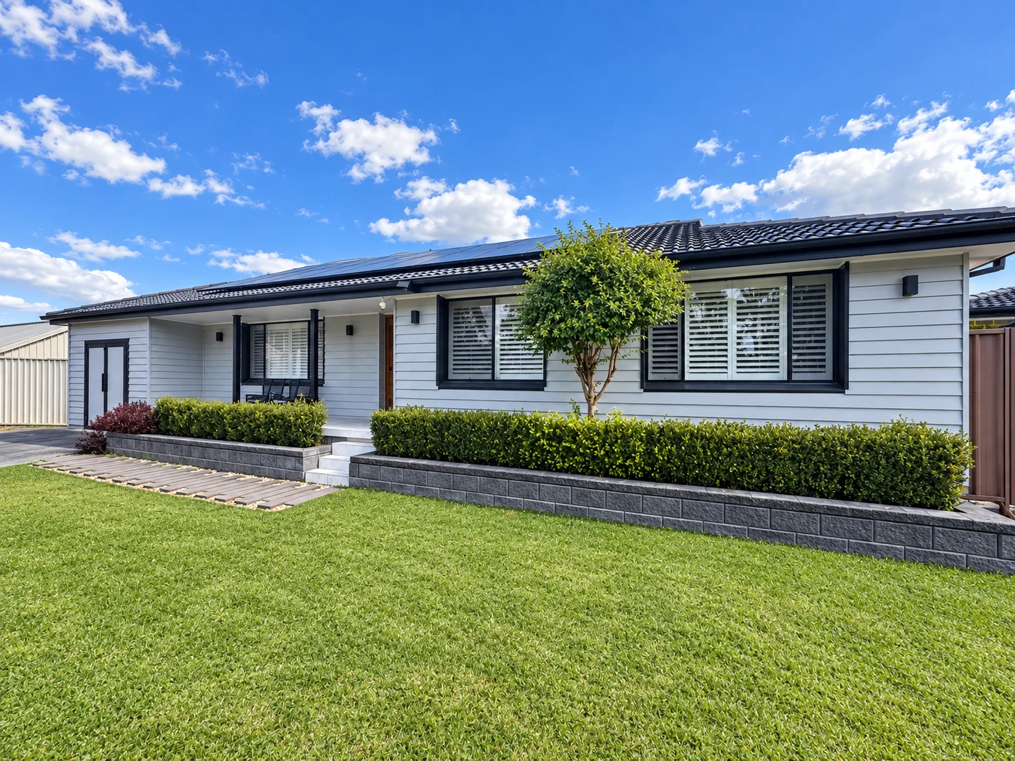 Completed single-storey home at Werrington County with light grey cladding, dark roof, solar panels, landscaped lawn and retaining walls under a bright blue sky